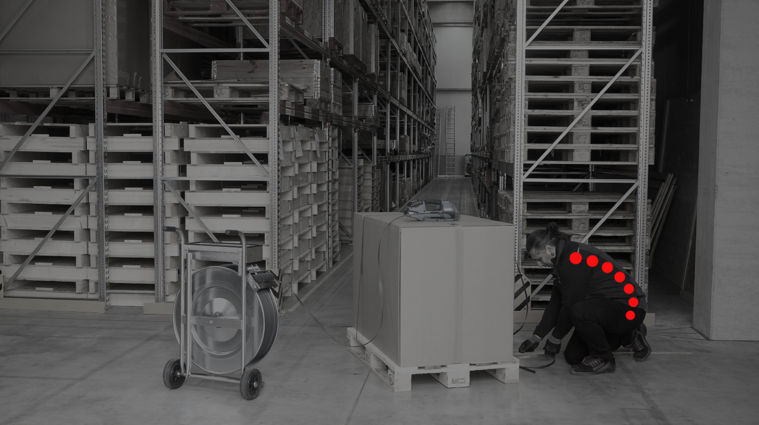 Ergonomische Umreifungsmaschine - Palettensicherung mit ErgoPack Umreifung einer Palette mit einem Abrollwagen. Die gekrümmte Haltung der Wirbelsäule ist rot markiert.